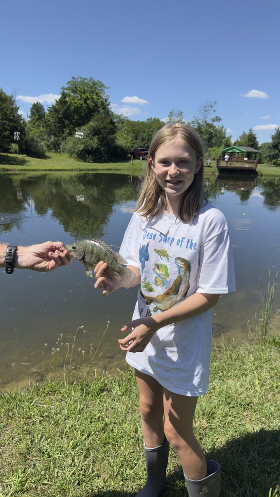 Girl holding a fish she just caught from the pond.
