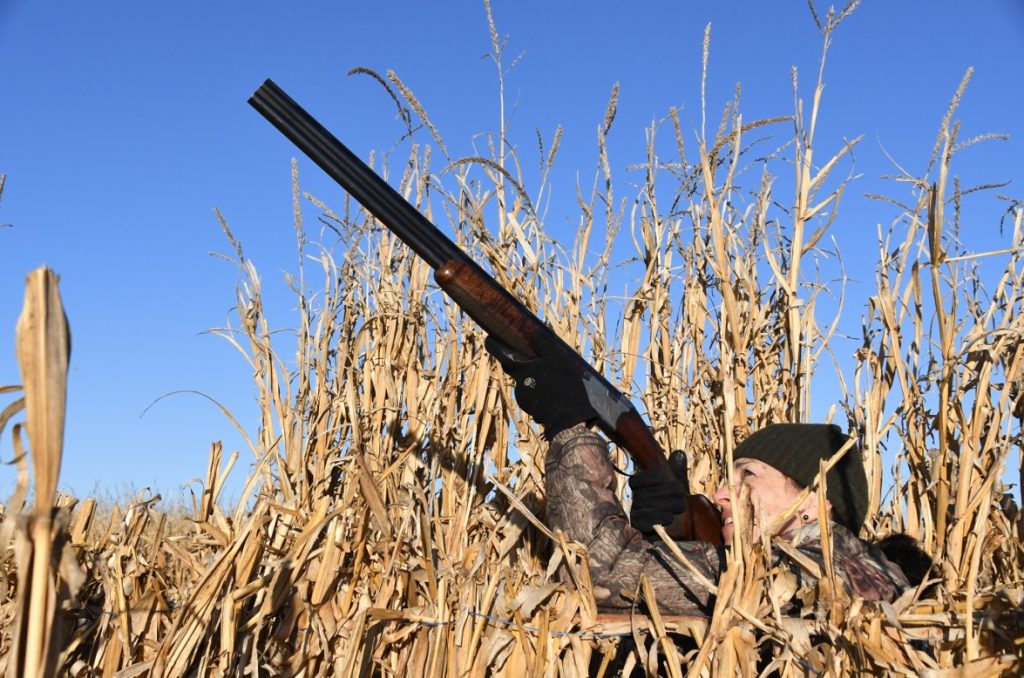Lisa Ballard pointing a gun in the air in a corn field.